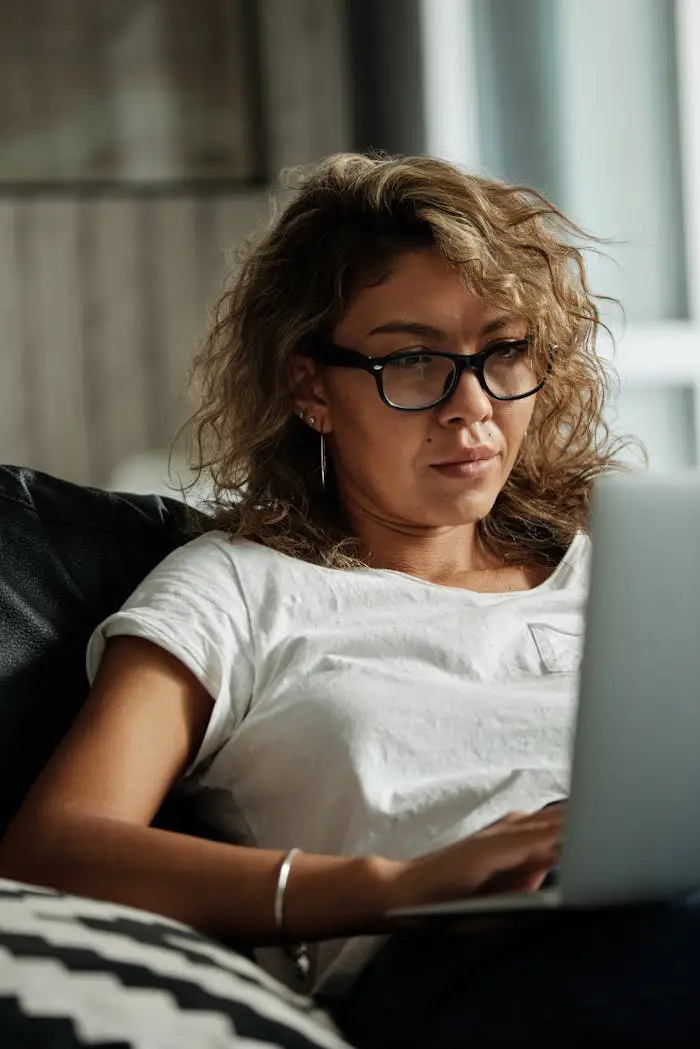 Young woman with glasses working on a laptop indoors, depicting remote work lifestyle.