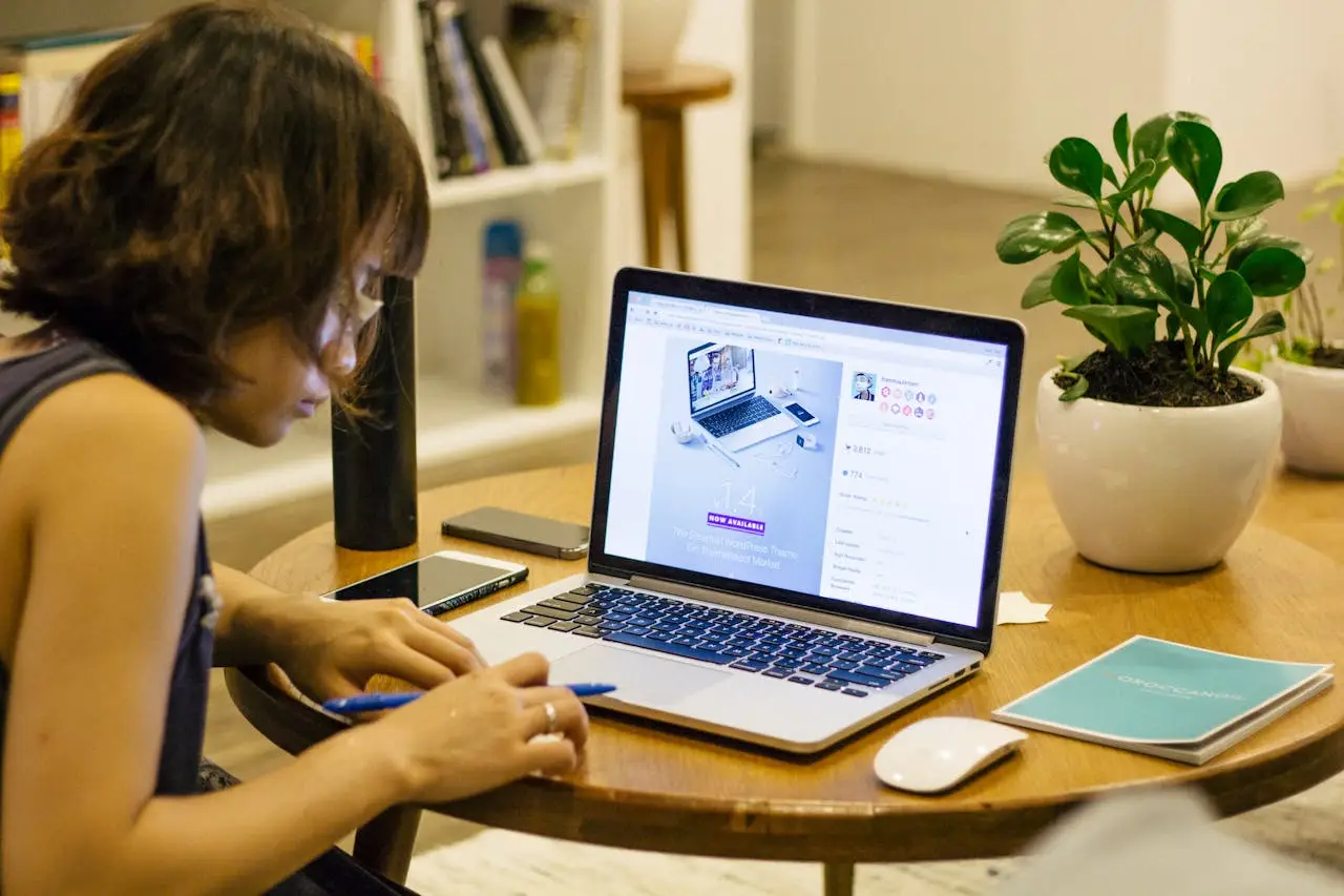 Woman working remotely from home with a laptop, pen, and plant on her desk, highlighting digital nomad lifestyle.